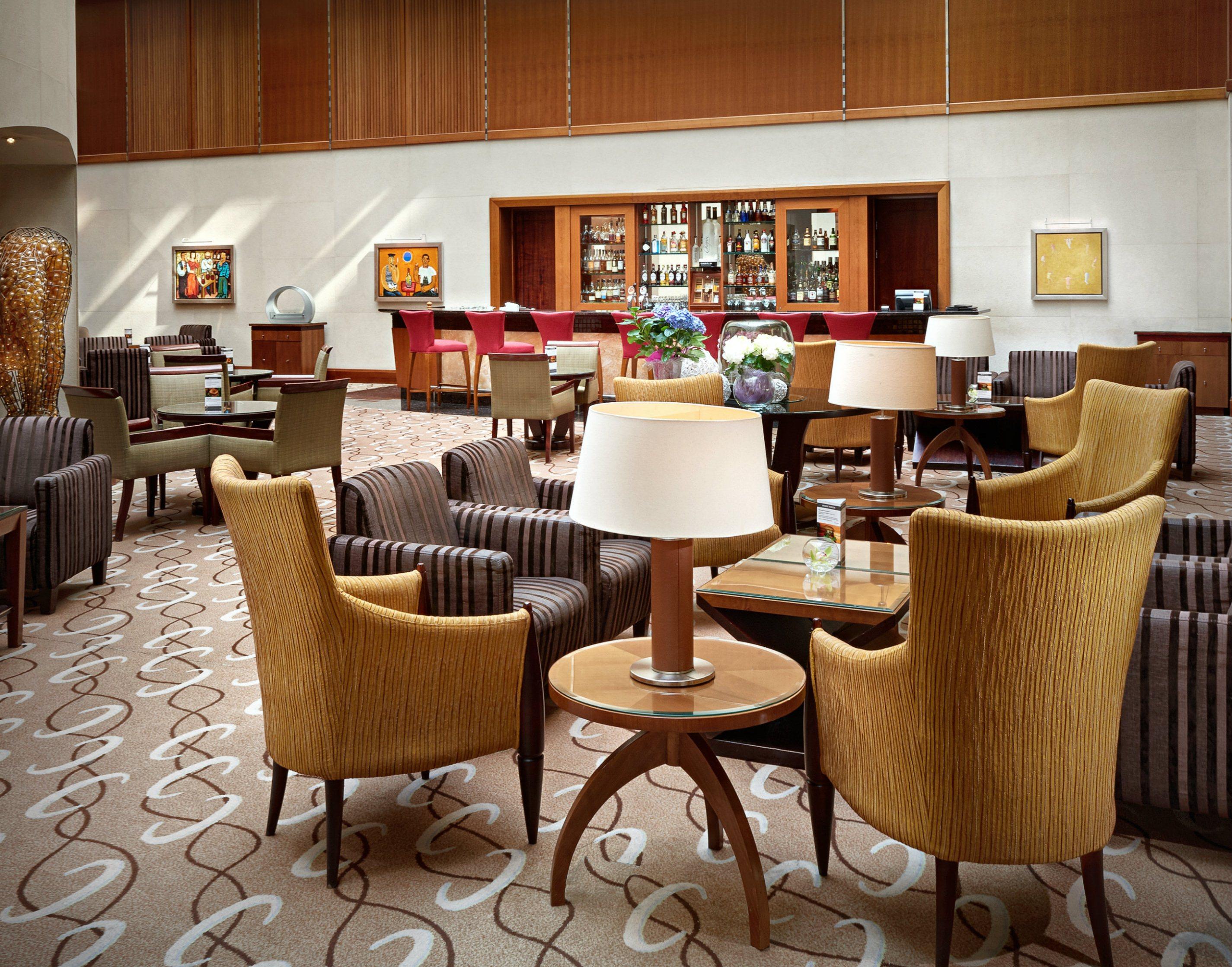 Regent Warsaw Hotel Buitenkant foto The photo shows a stylish and modern lounge area, likely within a hotel or upscale establishment. The seating consists of several chairs, predominantly in shades of brown and gold, arranged around small tables. A few lamps are placed on the tables, p