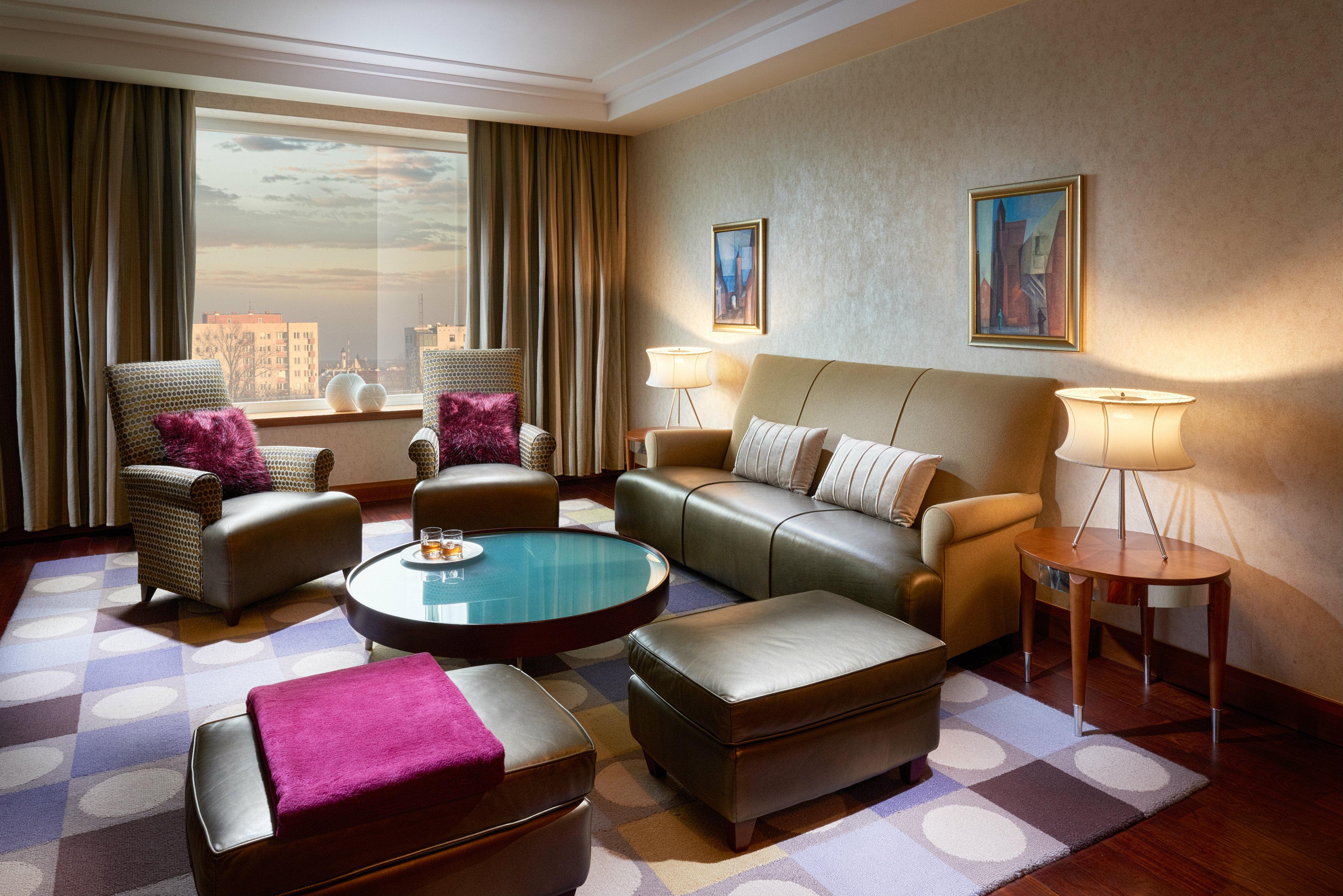 Regent Warsaw Hotel Buitenkant foto The photo shows a stylish and modern living room. It features a comfortable seating arrangement with a light brown leather sofa and two matching armchairs, each adorned with purple cushions. A round coffee table sits in the center, topped with a deco