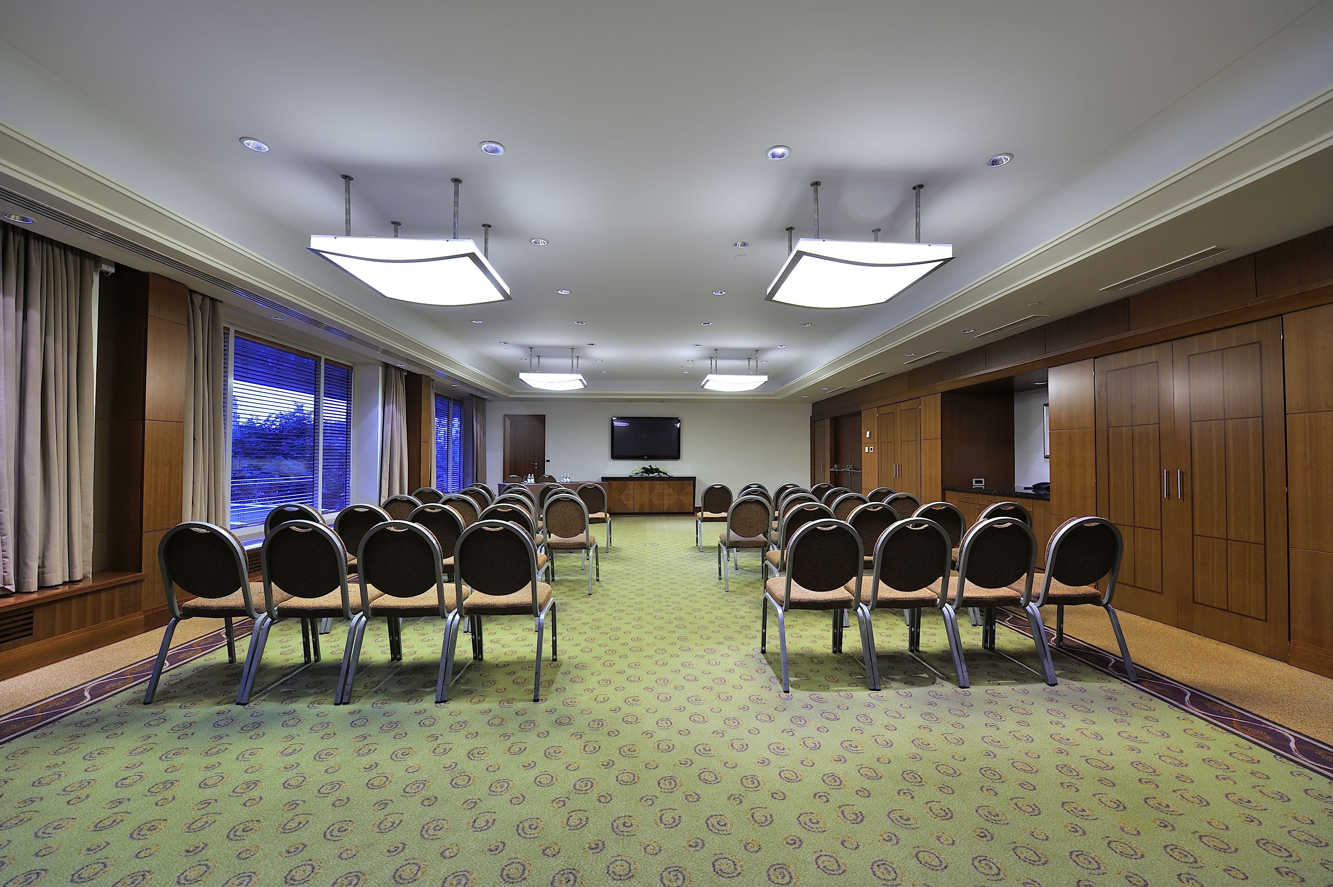 Regent Warsaw Hotel Buitenkant foto The photo shows a conference room or meeting space. It features several rows of chairs arranged in a semi-circle facing a wall-mounted television. The room has a carpeted floor with a patterned design and is illuminated by rectangular ceiling lights.