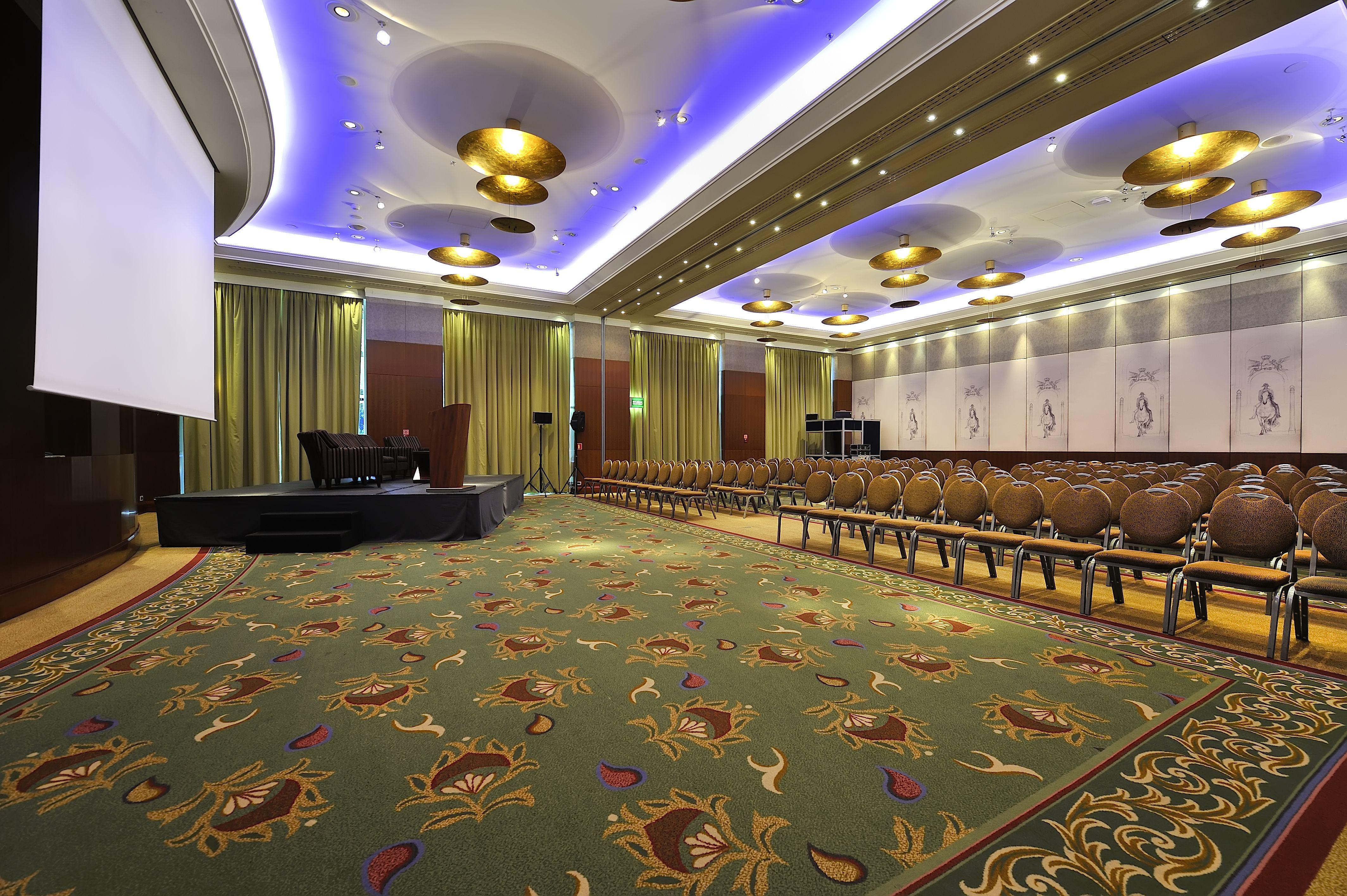 Regent Warsaw Hotel Buitenkant foto The photo depicts a spacious conference room or event space. The room features a decorative carpet with floral patterns and is arranged with rows of elegant, cushioned chairs. At the front of the room, there is a low platform or stage with seating, p