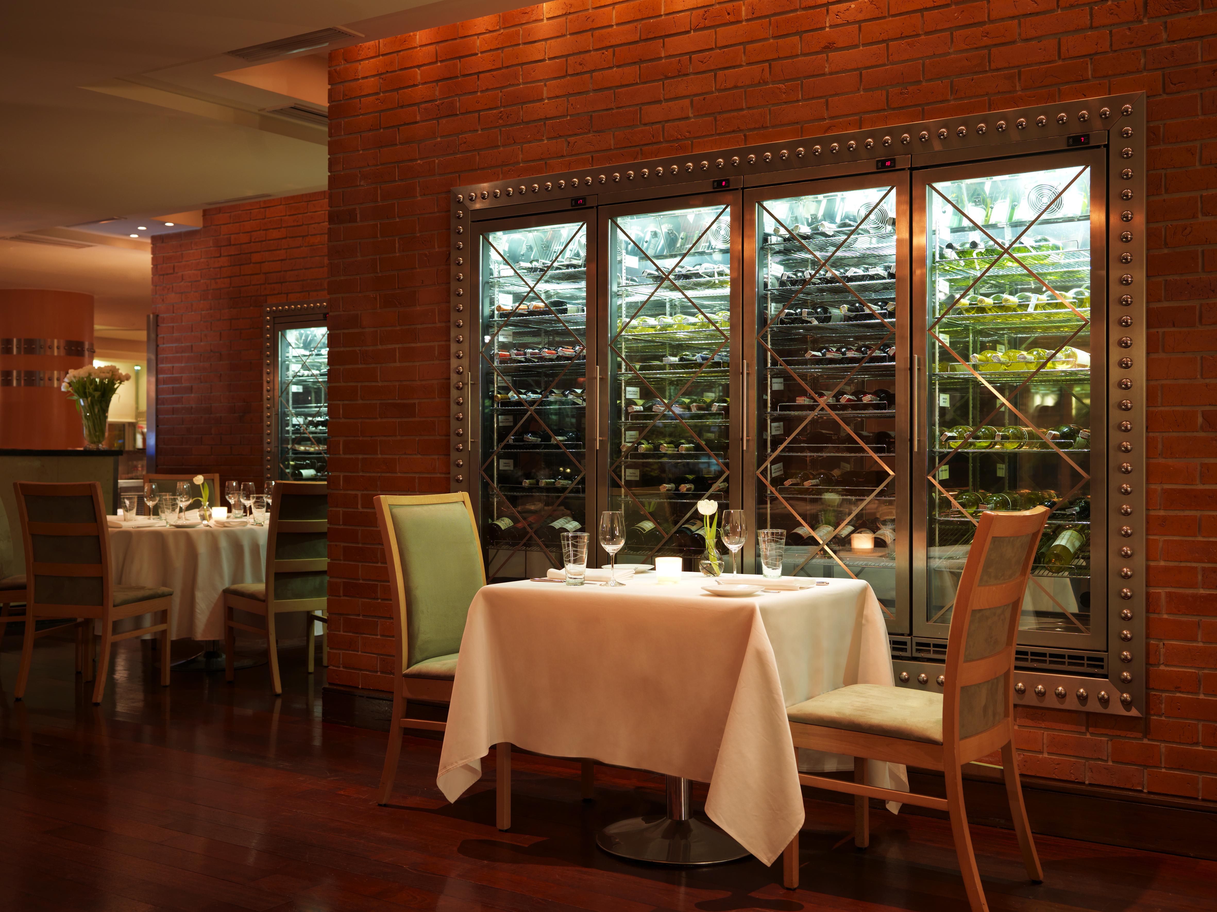 Regent Warsaw Hotel Buitenkant foto The photo shows an elegant dining setting in a restaurant. There are two tables, each elegantly set with white tablecloths and fine dining utensils, including glasses and plates. The ambiance is warm, with wooden flooring and a backdrop of exposed br