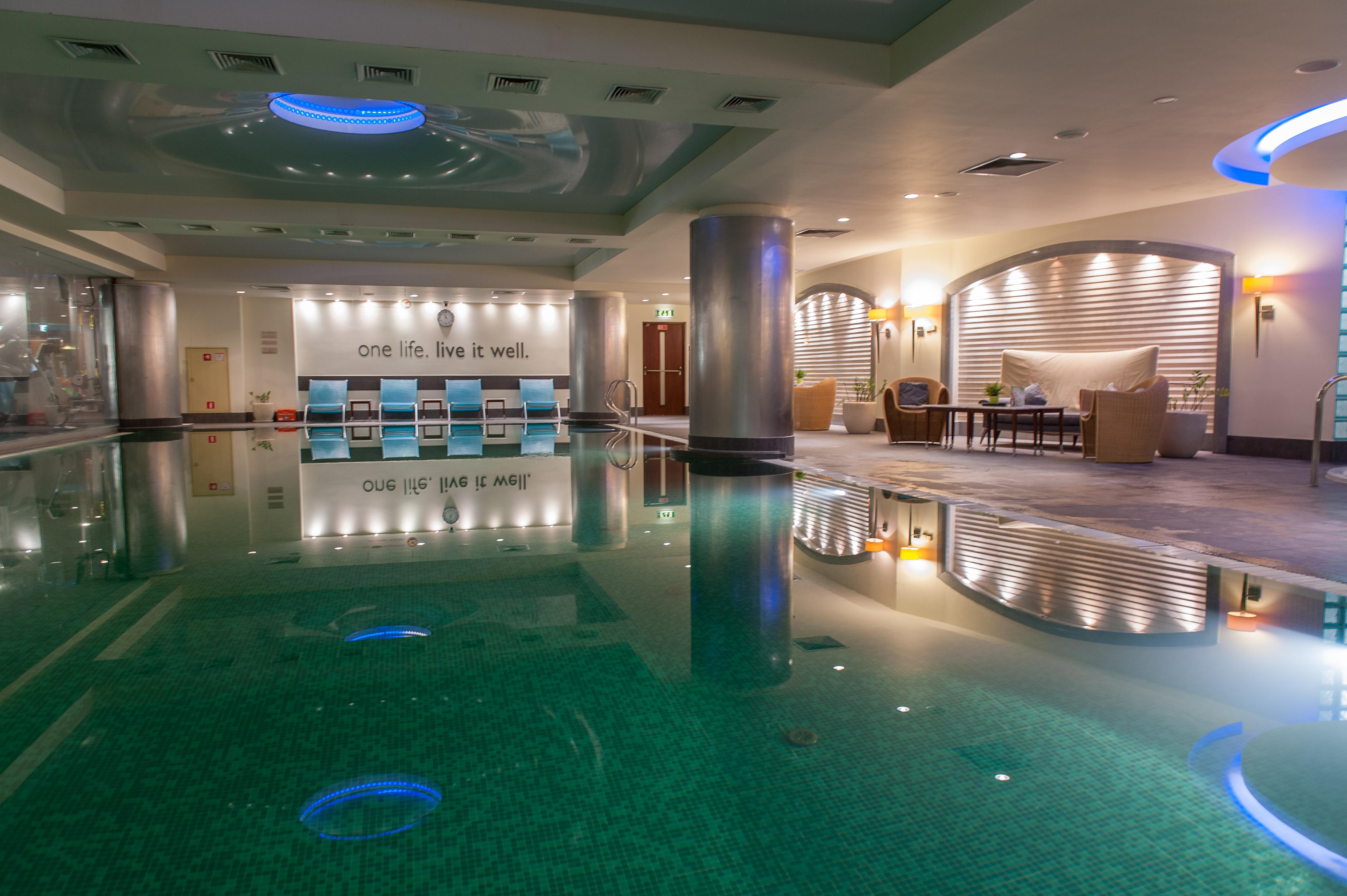 Regent Warsaw Hotel Buitenkant foto The photo depicts an indoor swimming pool area within a luxurious setting. The pool has a vibrant turquoise color, reflecting lights from the ceiling. Surrounding the pool are lounge chairs, and to one side, there is a seating area with comfortable c