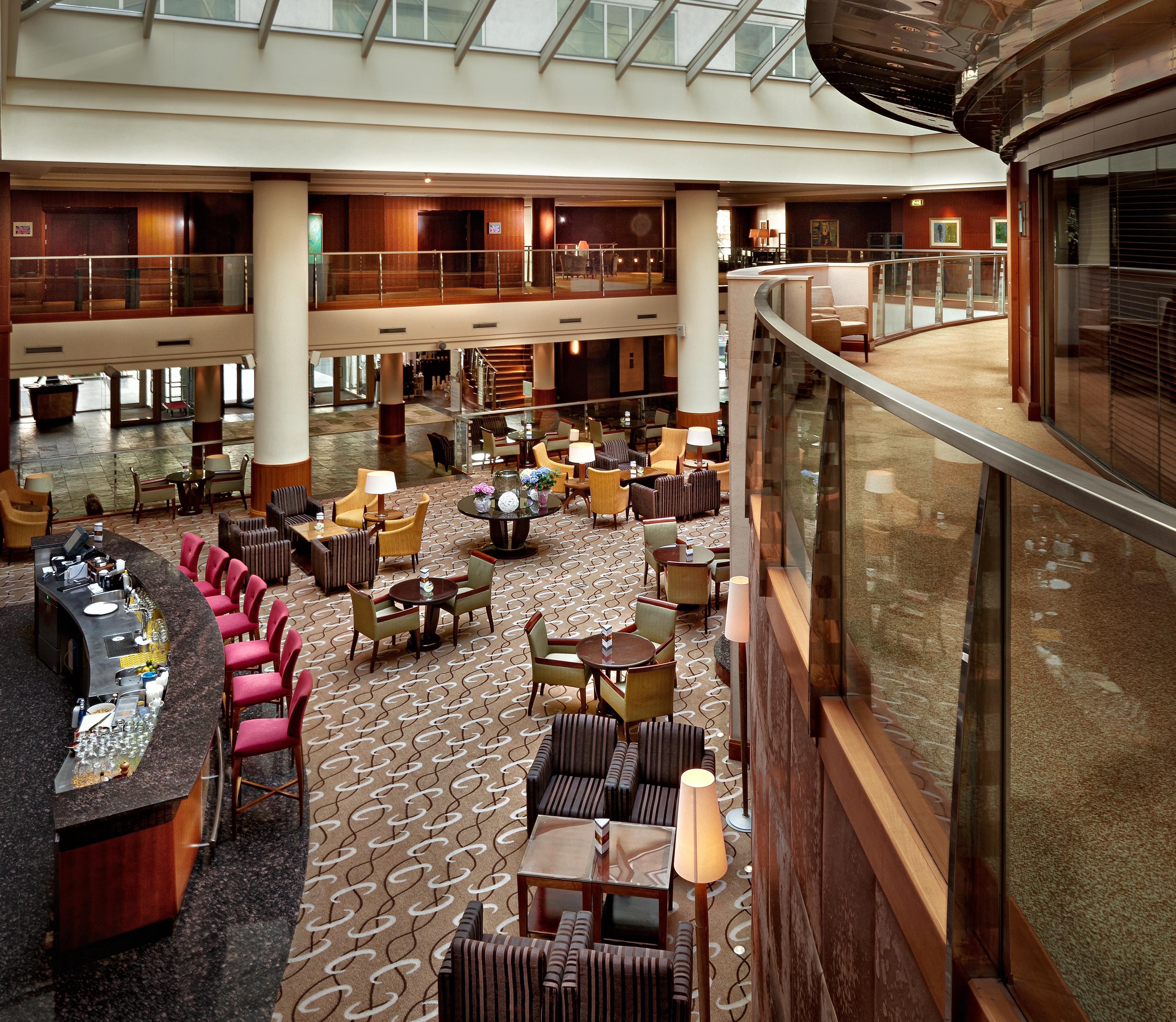 Regent Warsaw Hotel Buitenkant foto The photo shows the interior of a hotel lobby or lounge area. There are various seating arrangements with comfortable chairs and small tables. The layout appears open and spacious, with a curved balcony or walkway above. In the foreground, there is a