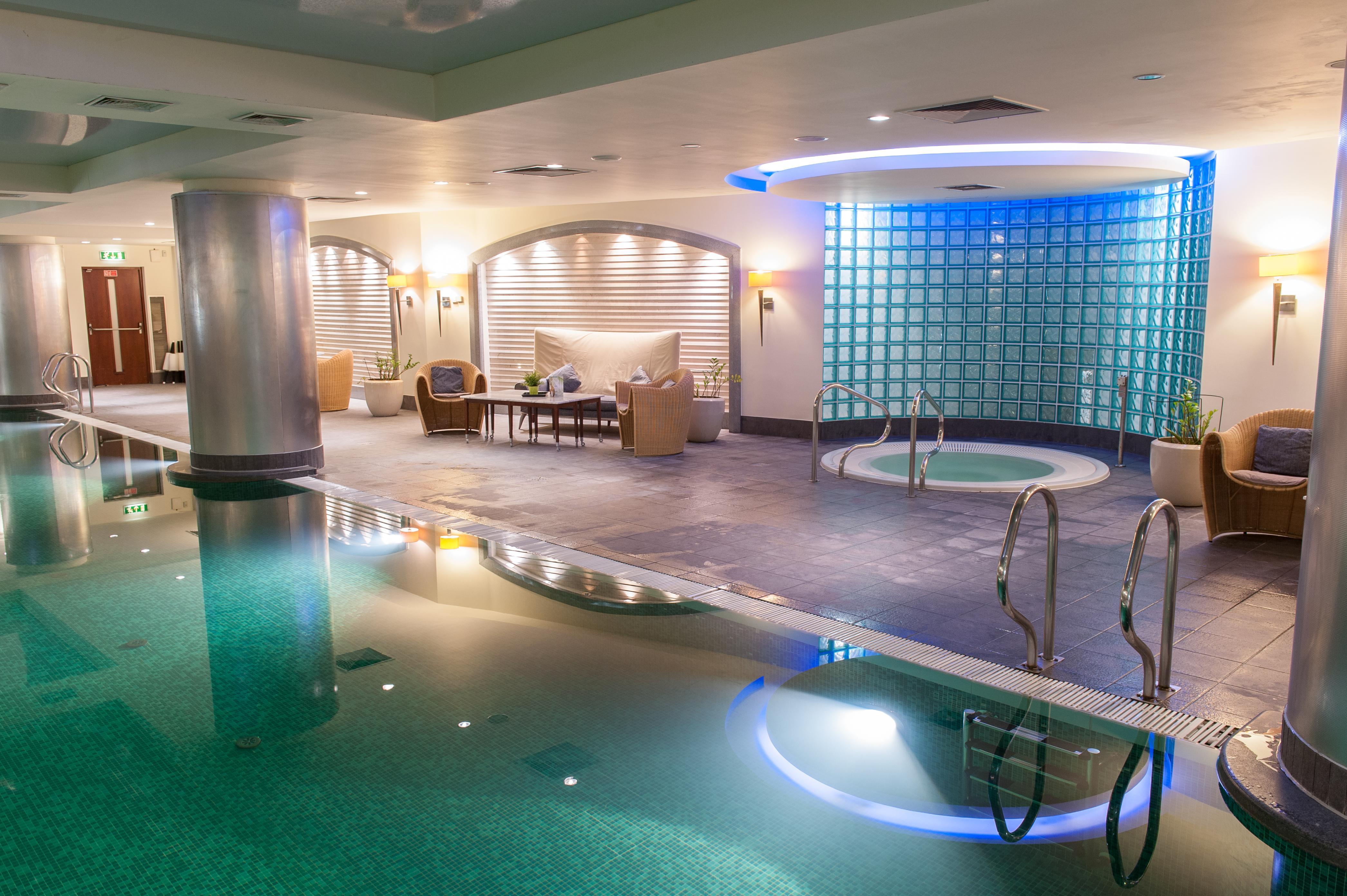 Regent Warsaw Hotel Buitenkant foto The photo shows a spa area featuring a calm and relaxing atmosphere. There is a swimming pool with clear water reflecting the soft lighting. To one side, there is a hot tub with steps leading into it. The walls are adorned with light-colored material