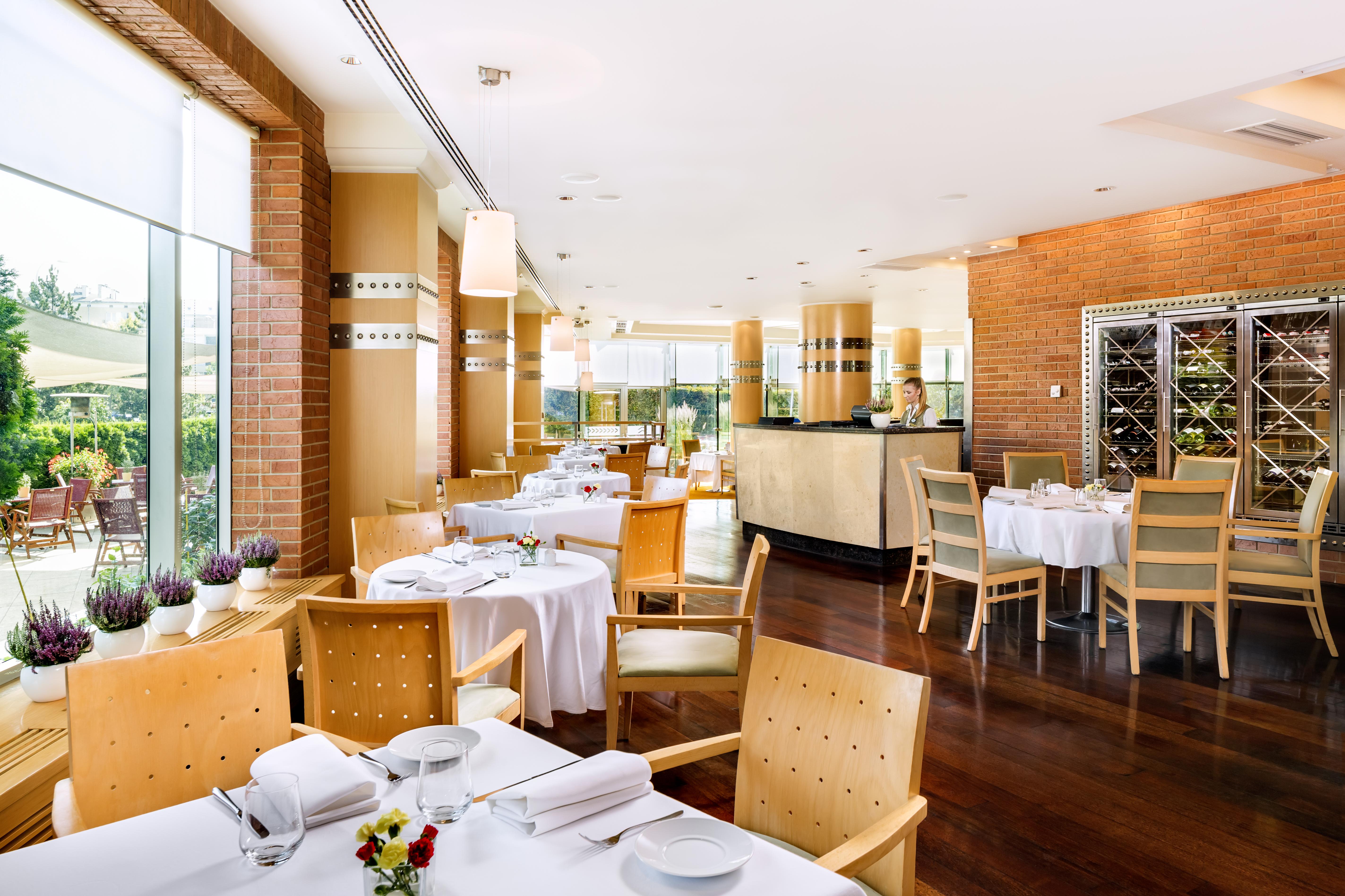 Regent Warsaw Hotel Buitenkant foto The photo shows a modern, elegantly designed restaurant interior. It features wooden flooring and a warm color palette with brick walls and soft lighting. Tables are set with white tablecloths and neatly arranged dishes and cutlery. There are wooden 
