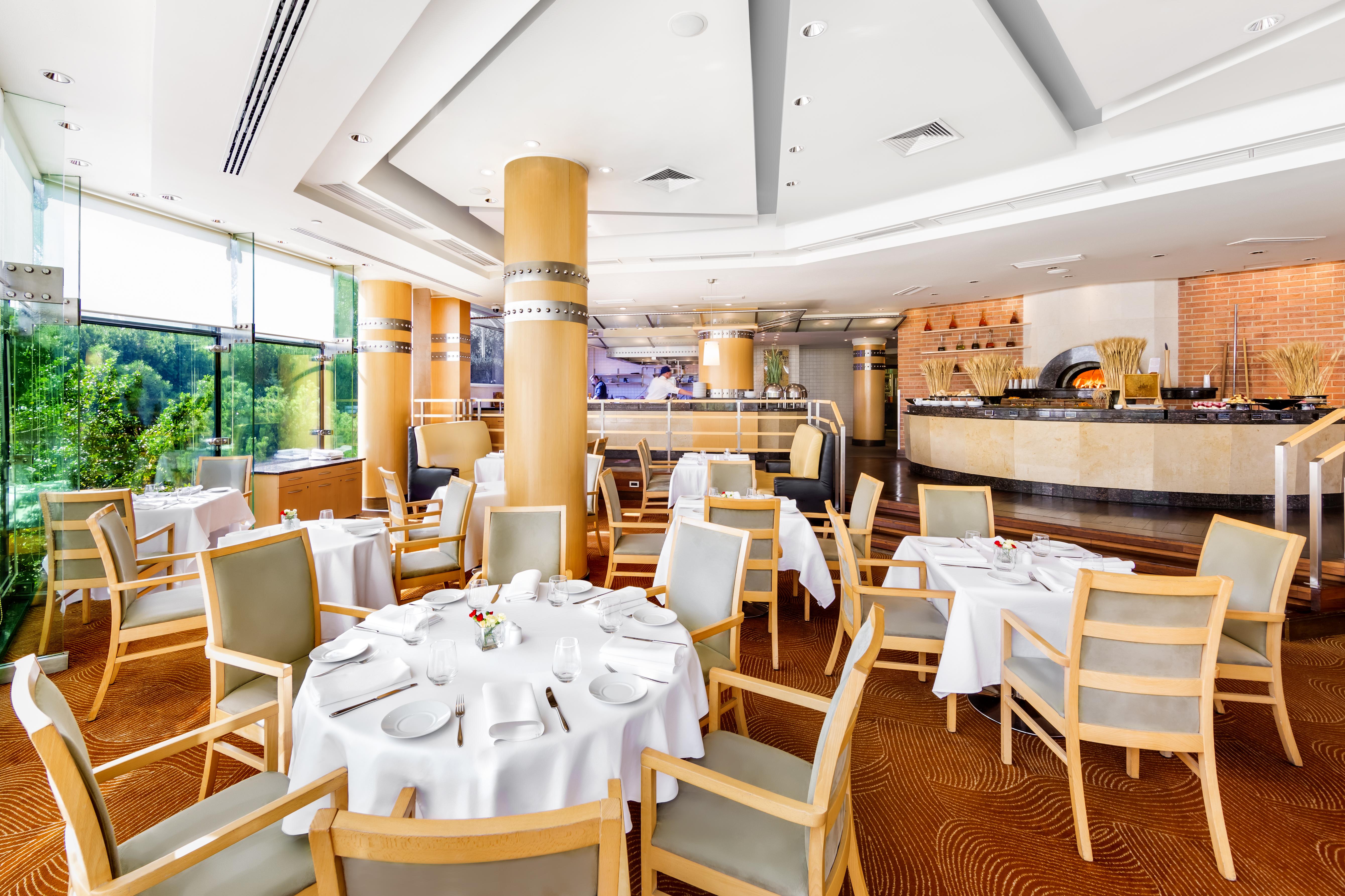 Regent Warsaw Hotel Buitenkant foto The photo shows an elegant dining area within a restaurant. There are multiple round tables covered with white tablecloths, each set with plates and cutlery, indicating a formal dining setup. The chairs are made of light-colored wood with soft cushio