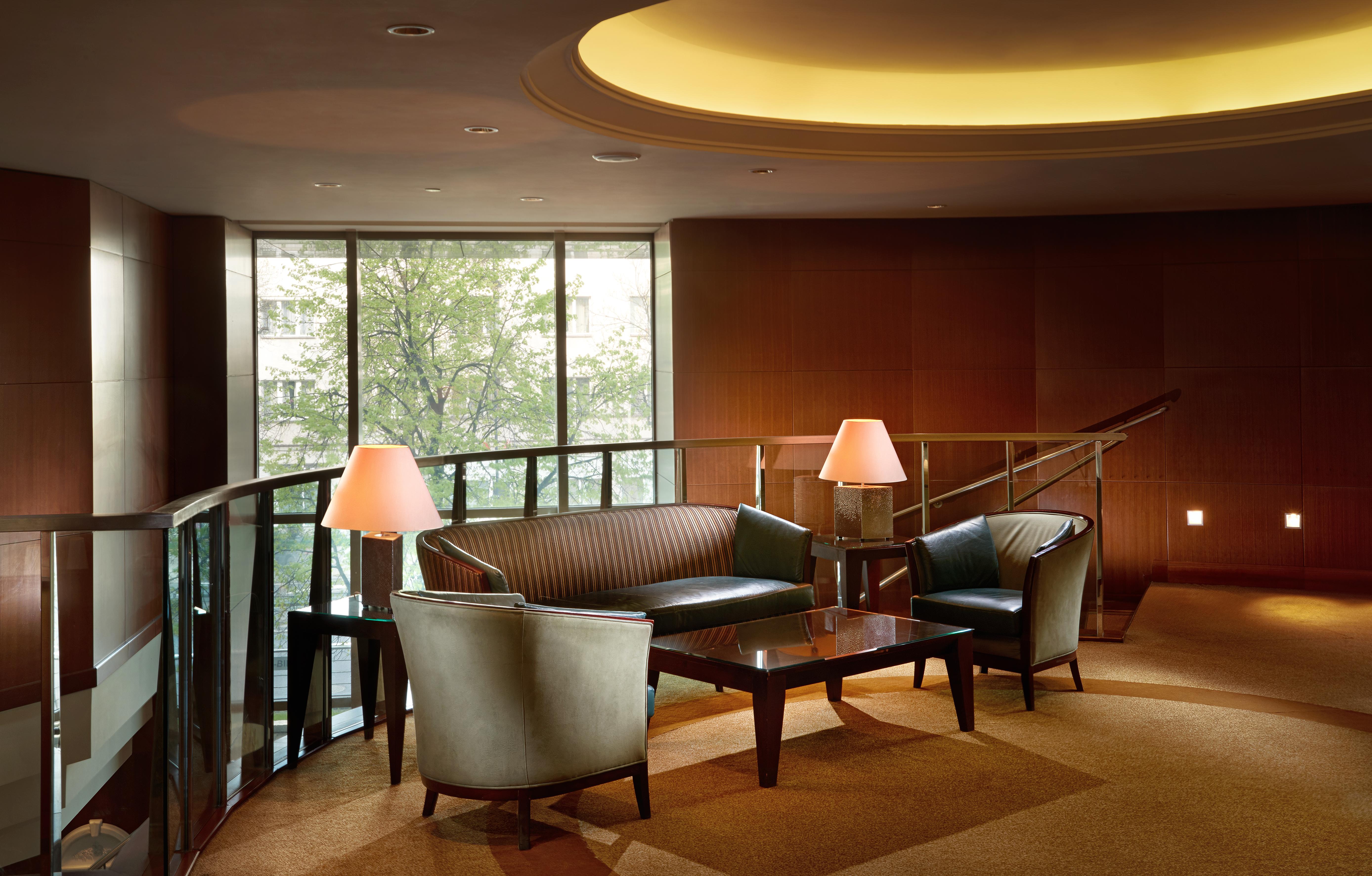Regent Warsaw Hotel Buitenkant foto The photo depicts a modern lounge area. It features a curved seating arrangement with a dark, leather couch and two matching armchairs. A sleek coffee table is placed in the center, and there are two lamps providing soft lighting. The space is enhanc