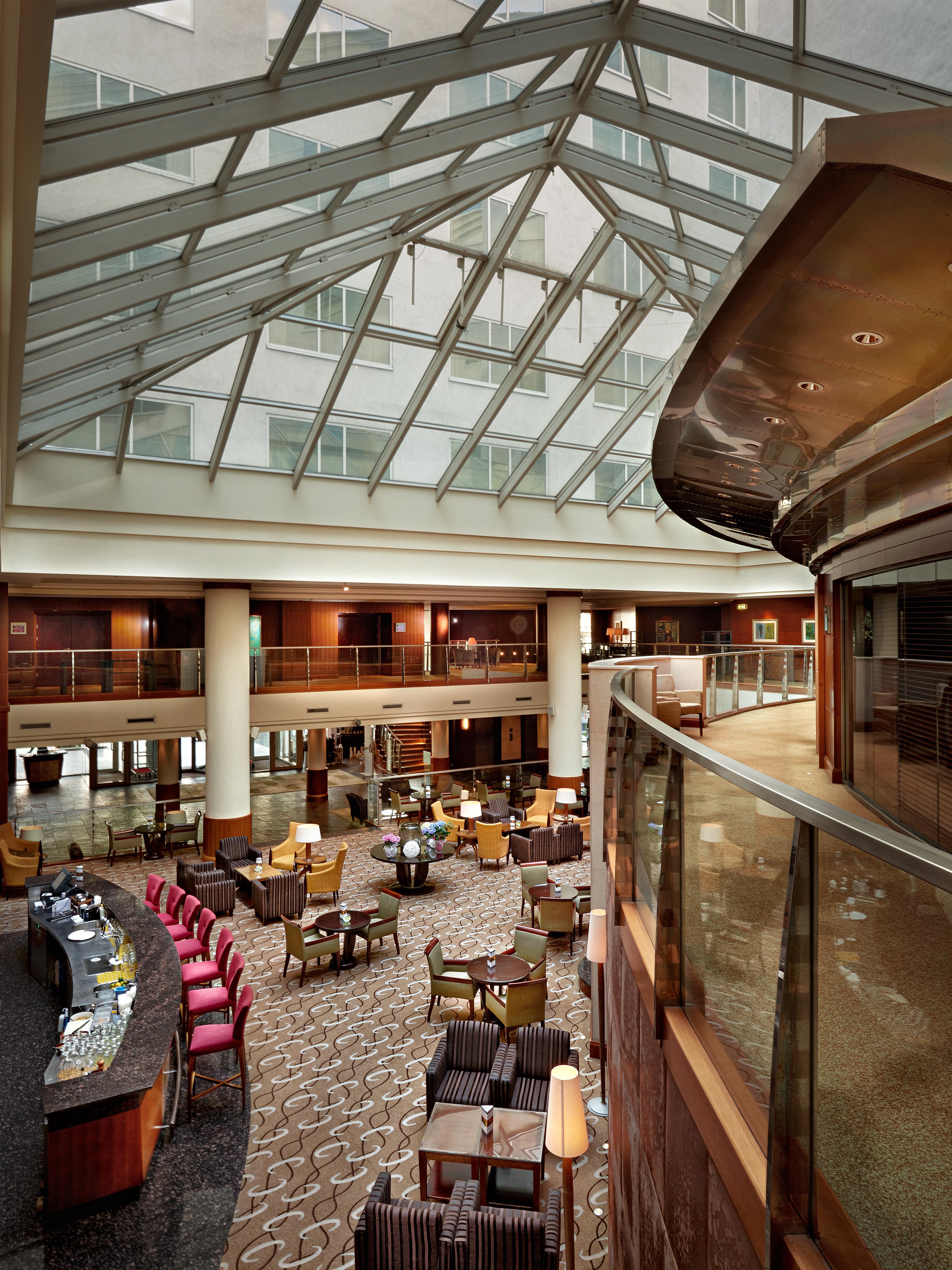 Regent Warsaw Hotel Buitenkant foto The photo depicts a spacious interior of a hotel lobby or atrium. It features a contemporary design with a high glass ceiling that allows natural light to flood the space. The area is furnished with comfortable seating arrangements, including armchai