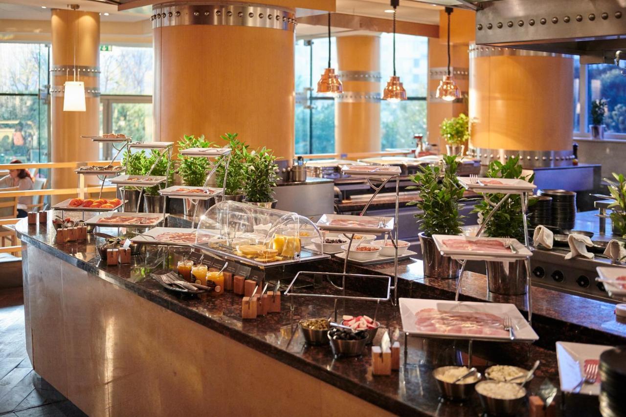 Regent Warsaw Hotel Buitenkant foto The photo shows a buffet setup in a restaurant or dining area. There is a long counter featuring various food items displayed in trays and covered with glass domes. The table is adorned with small potted plants, adding a touch of greenery to the spac