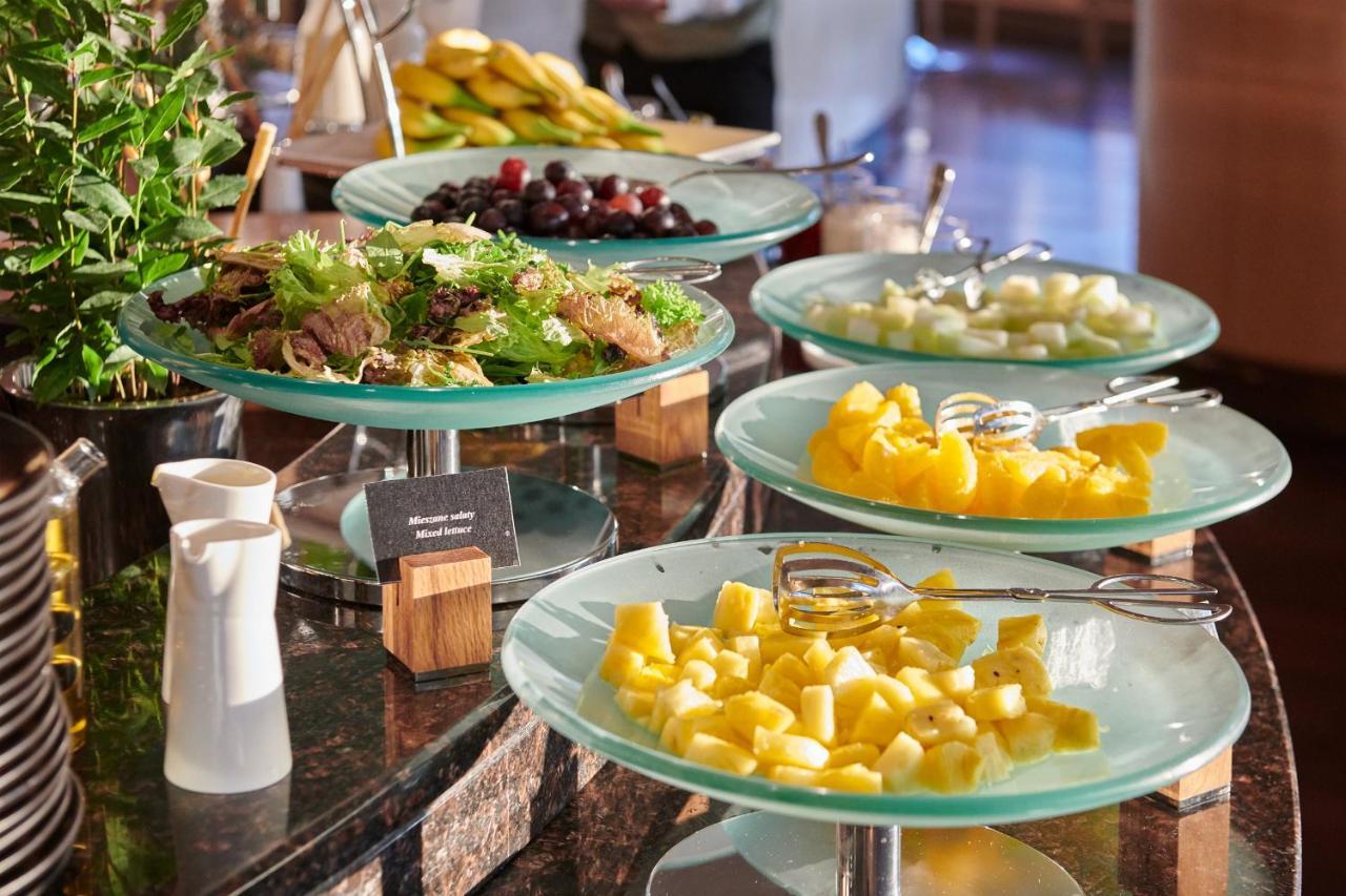 Regent Warsaw Hotel Buitenkant foto The photo displays a buffet-style setup featuring a variety of food items. There are several glass trays stacked on a countertop, each holding different types of food. 

1. **Fresh Vegetables and Fruit:** One tray appears to have a mix of leafy green