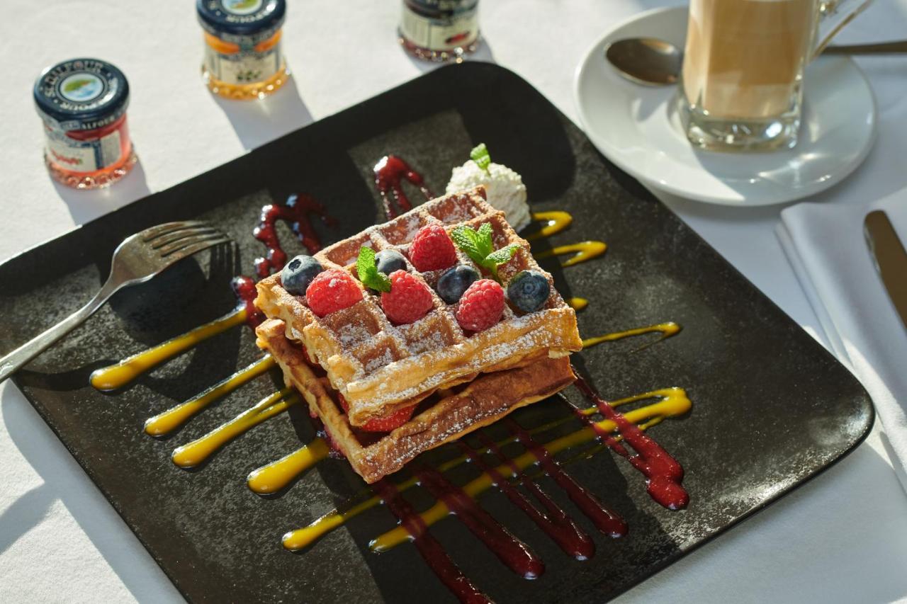 Regent Warsaw Hotel Buitenkant foto The photo features a delicious plate of waffles topped with a variety of fresh berries, including raspberries and blueberries. The waffles are dusted with powdered sugar and accompanied by a dollop of whipped cream. The plate is artistically arranged
