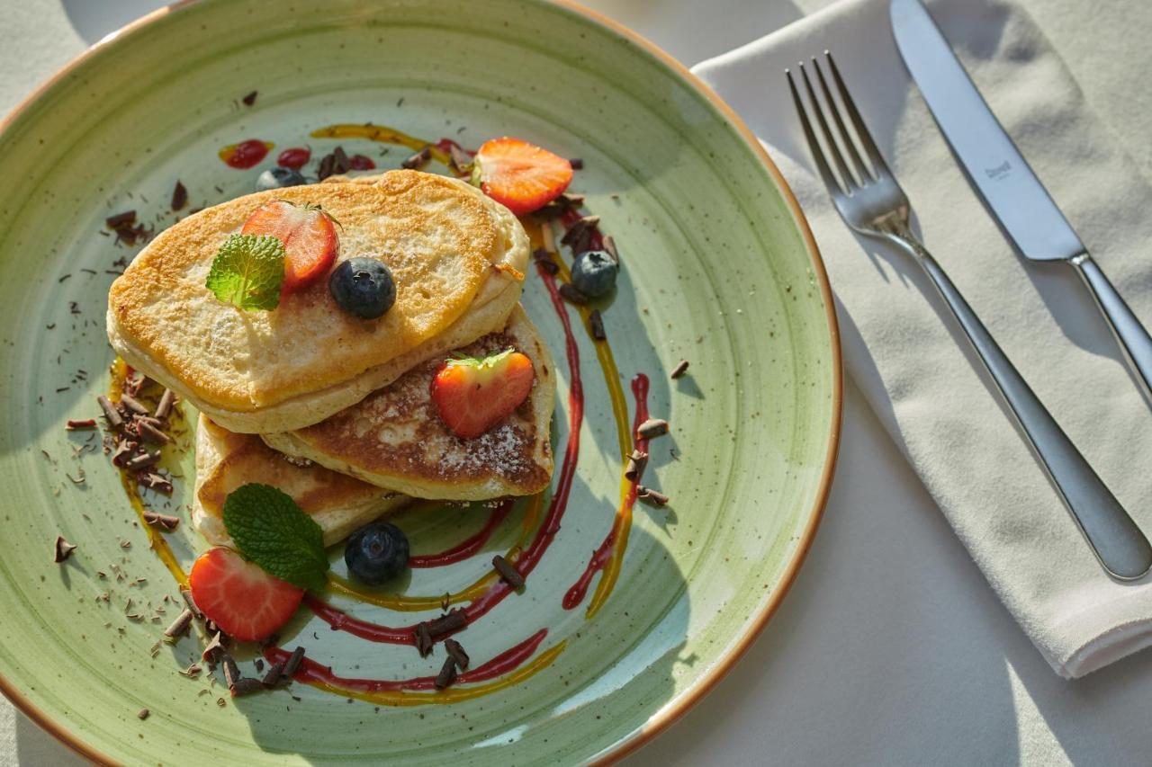 Regent Warsaw Hotel Buitenkant foto The photo shows a plate of pancakes stacked on top of each other. The pancakes are garnished with fresh strawberries, blueberries, and mint leaves. There are drizzles of syrup and chocolate around the pancakes, adding a colorful touch to the presenta
