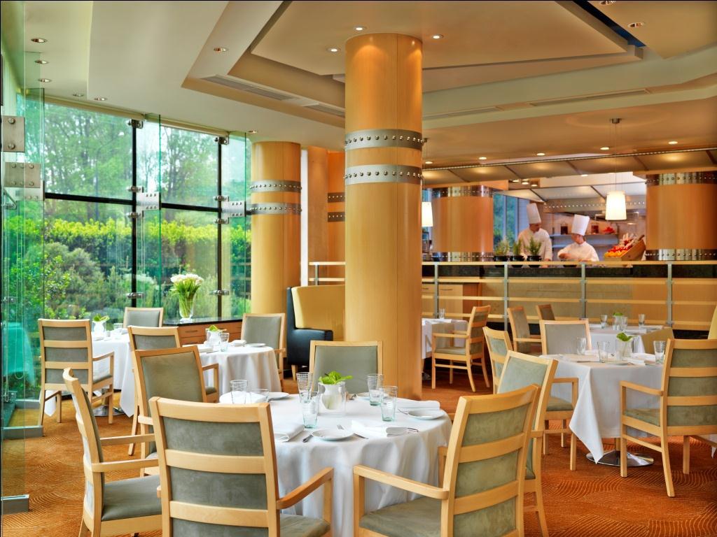 Regent Warsaw Hotel Buitenkant foto The photo shows an elegant restaurant interior. It features stylish wooden chairs around neatly set tables, which are adorned with white tablecloths and glassware. Large windows allow natural light to fill the space, providing a view of the greenery 