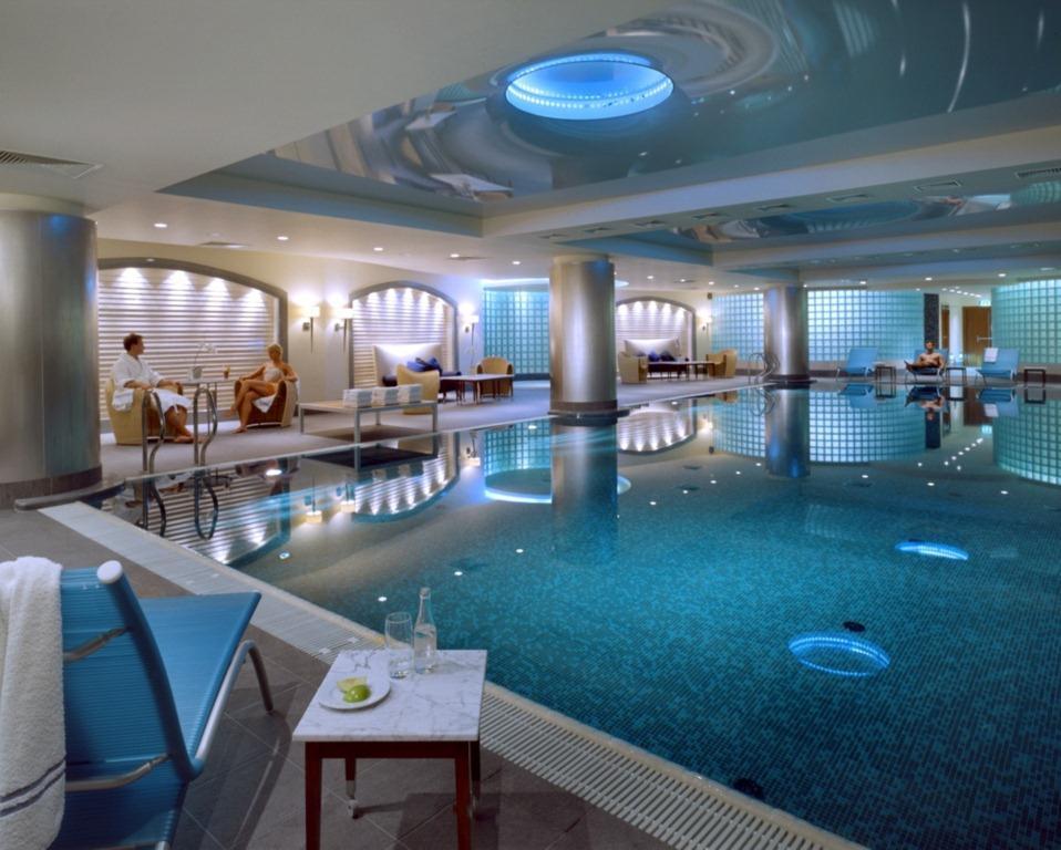 Regent Warsaw Hotel Faciliteiten foto The photo shows a luxurious indoor swimming pool area. The pool has a sparkling blue water surface, and its surroundings are designed with sleek, contemporary architecture. The lighting is soft, with blue accents illuminating the space. On one side, 